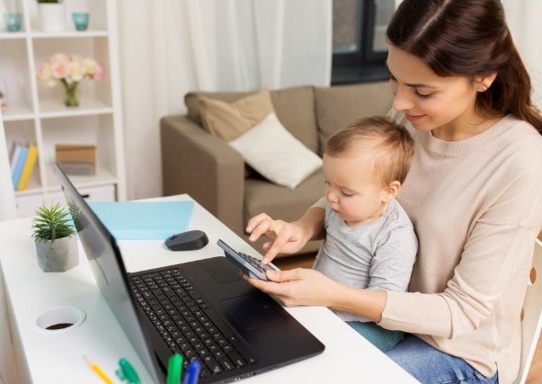 A woman using a calculator and laptop with her baby.